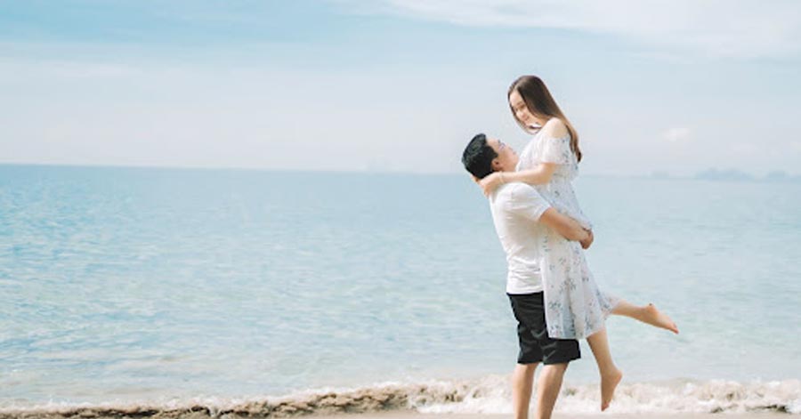 A man lifting his beautiful partner on the beach.